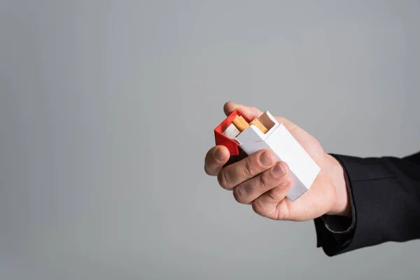 Обрезанный вид мужской руки с пачкой сигарет, изолированных на сером — стоковое фото
