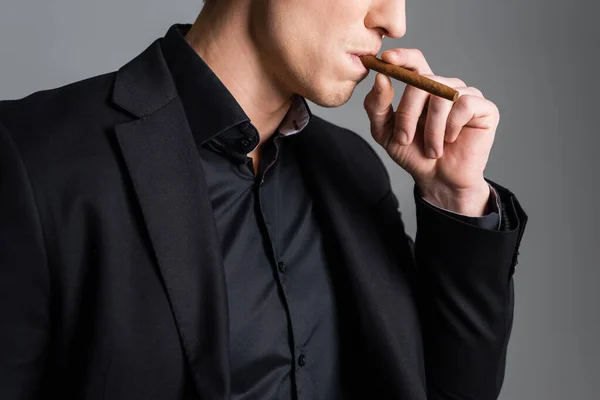 Partial view of man in black blazer smoking cigar isolated on grey — Photo de stock