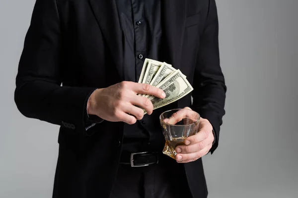 Ausgeschnittene Ansicht eines Mannes in schwarzer Festkleidung mit Whiskey und Dollars isoliert auf Grau — Stockfoto