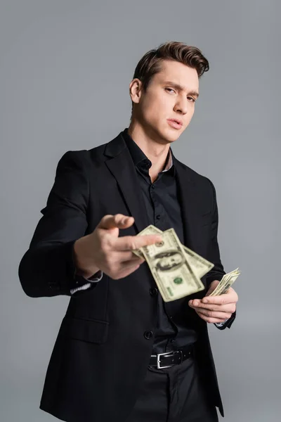 Confident man in formal wear showing blurred dollars at camera isolated on grey — Photo de stock