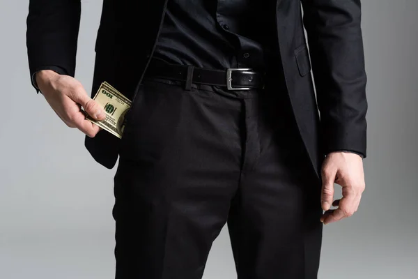 Обрезанный вид человека в черном костюме, держащего деньги возле кармана, изолированного на сером — стоковое фото