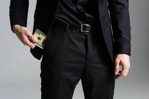 Cropped view of man in black suit holding money near pocket isolated on grey — Stockfoto