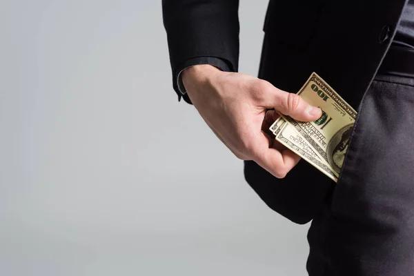 Обрезанный вид человека, держащего доллары возле кармана, изолированного на сером — стоковое фото