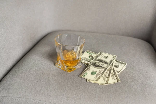 Стакан виски и долларовые купюры на сером кресле — стоковое фото
