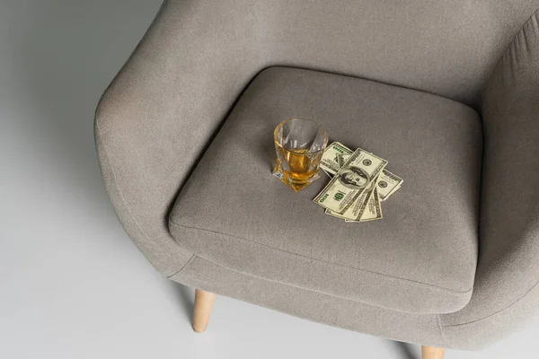 Вид на долларовые купюры и стакан виски на сером кресле — стоковое фото