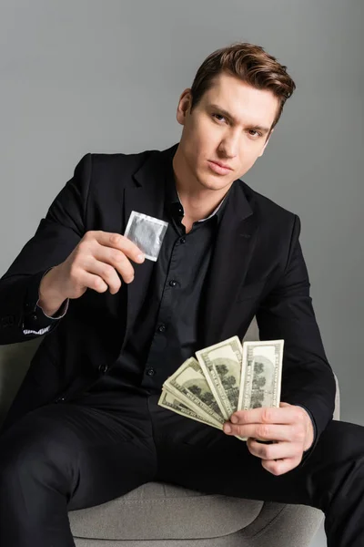 Homme confiant tenant préservatif et dollars tout en regardant la caméra isolée sur gris — Photo de stock