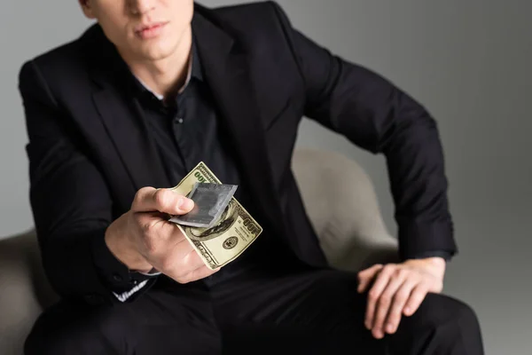 Cropped view of blurred man holding condom and dollar banknote isolated on grey — Fotografia de Stock