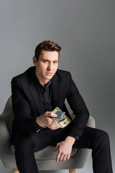 Man in black suit holding condom and money while looking at camera isolated on grey — Stock Photo