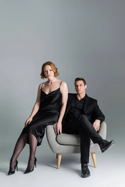 In voller Länge von selbstbewussten Mann und Frau posiert in der Nähe Sessel auf grauem Hintergrund — Stockfoto