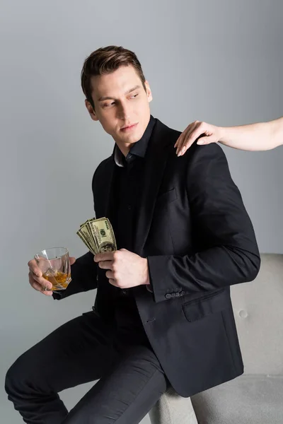 Woman touching shoulder of man with whiskey and dollar banknotes isolated on grey — Stock Photo