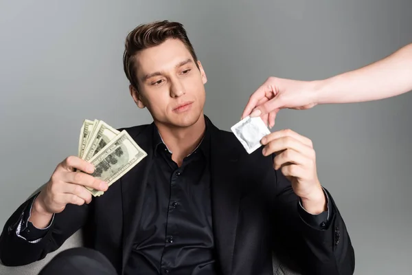 Mann in offizieller Kleidung hält Dollars und Kondom in der Nähe von Frau isoliert auf grau — Stockfoto