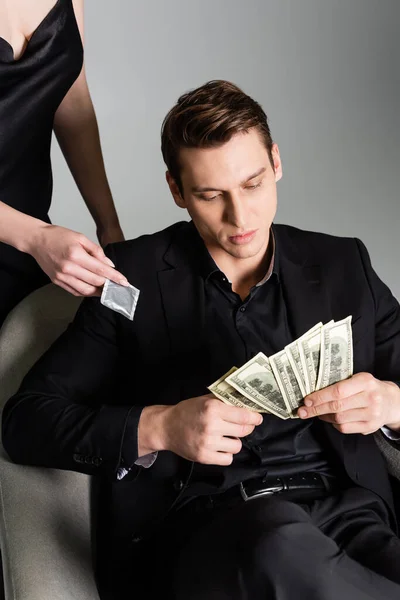 Mann im schwarzen Anzug zählt Geld neben Frau mit Kondom isoliert auf grau — Stockfoto