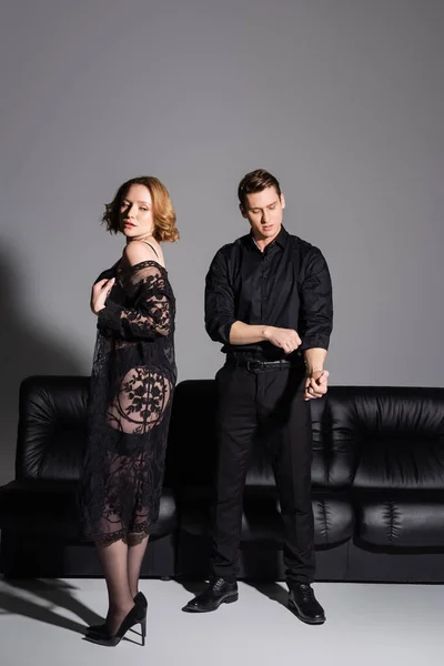 Man in black formal wear near sensual woman in lace tunic on grey background - foto de stock