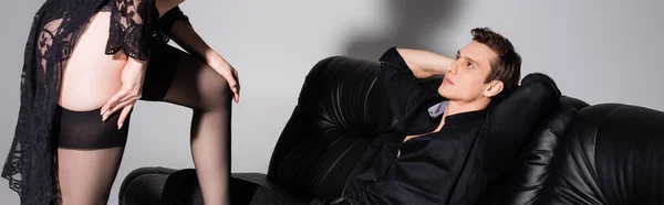 Man with hands behind head looking at sexy woman in black stockings isolated on grey, banner — Stock Photo