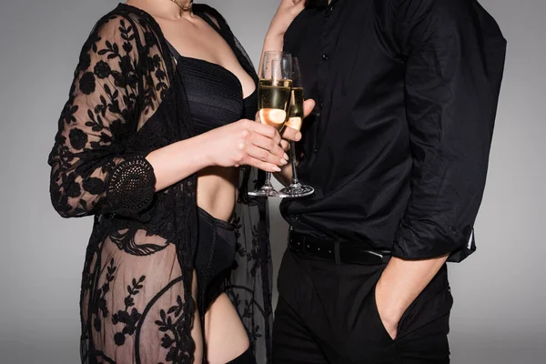 Cropped view of woman in lace tunic clinking champagne glasses with man isolated on grey — Stock Photo