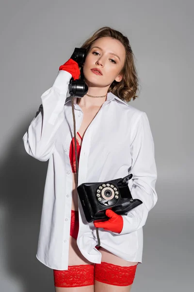 Seductive woman in white shirt and red gloves talking on telephone on grey background - foto de stock