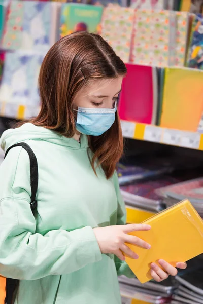 Child in medical mask looking at new notebook in stationery shop — Stock Photo