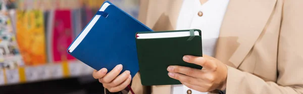 Cropped view of woman holding new notepads in stationery shop, banner — Stockfoto