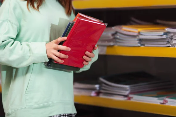 Cropped view of child holding multicolored copybooks in store - foto de stock