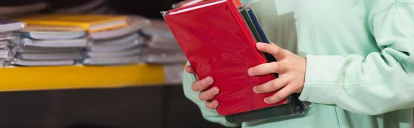 Cropped view of child holding colorful copybooks in stationery store, banner — Stockfoto