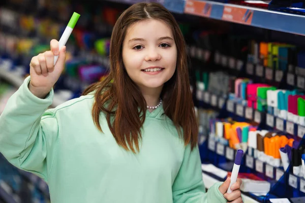 Весела дівчина дивиться на камеру, тримаючи повстяні ручки в канцелярському магазині — стокове фото