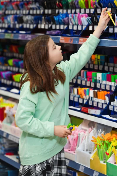 Mädchen wählt Schulbedarf auf Regal im Schreibwarengeschäft — Stockfoto