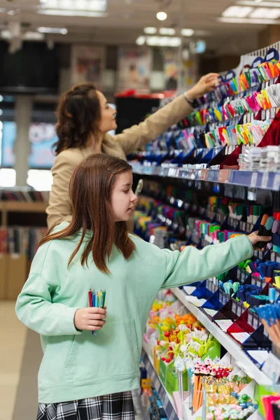 Girl with new pens choosing school supplies near blurred mom in stationery store — Stockfoto