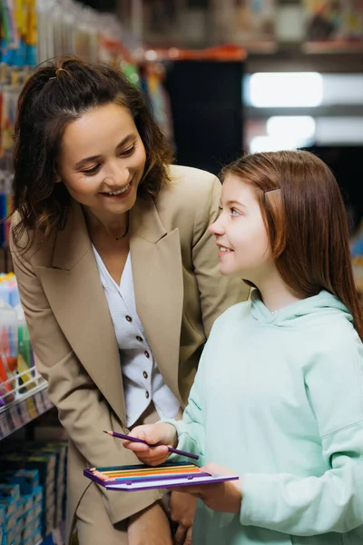 Дитина з набором кольорових олівців, дивлячись на щасливу маму в канцелярському магазині — стокове фото