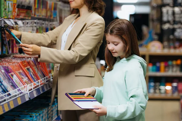 Дівчина тримає набір кольорових олівців біля матері в магазині канцелярських товарів — стокове фото
