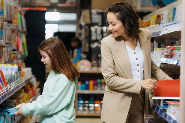 Sorrindo mulher e menina escolhendo novos materiais escolares na papelaria — Fotografia de Stock