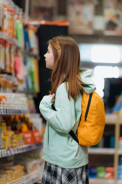 Side view of girl with backpack in blurred stationery store — Stock Photo