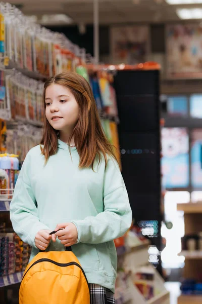 Дівчина з рюкзаком стоїть в розмитому канцелярському магазині — стокове фото