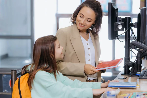 Woman with daughter smiling at each other at cash desk in stationery store — Stockfoto