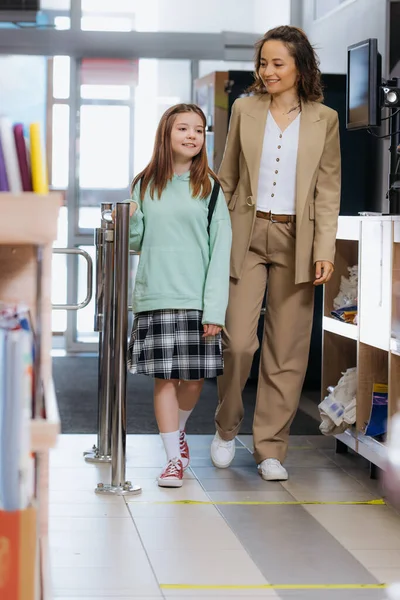 Full length of happy mother and daughter entering stationery store — стоковое фото