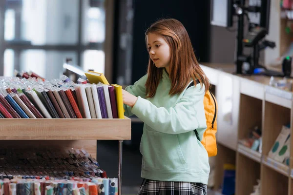 Schoolgirl choosing from variety of copybooks in stationery store — стоковое фото