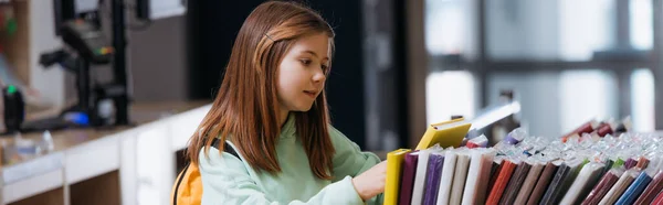 Schoolgirl choosing from different notebooks in stationery shop, banner — стоковое фото