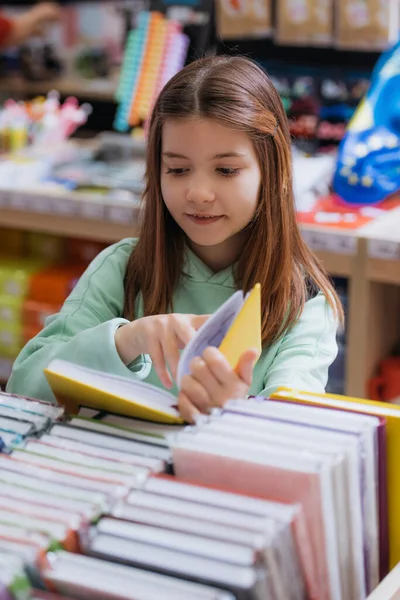 Усміхнена школярка вибирає книгу в магазині канцелярських товарів — стокове фото