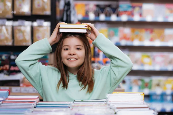 Cheerful girl holding new notebooks above head and looking at camera — Stockfoto