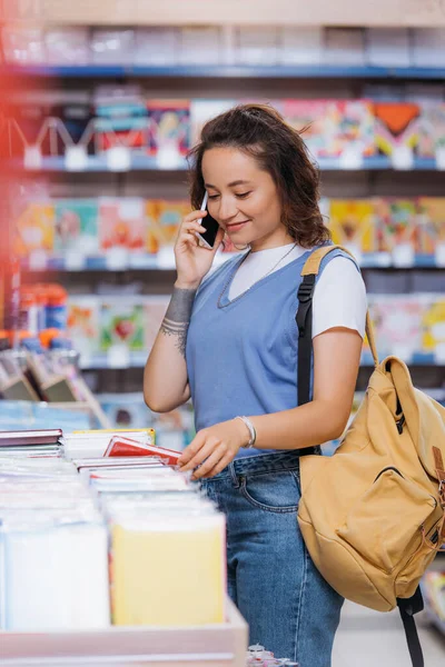 Lächelnde Frau, die mit dem Handy telefoniert, während sie aus einer Vielzahl von Werbetexten im Geschäft auswählt — Stockfoto