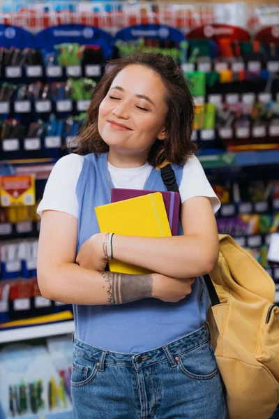 Pleased student with closed eyes hugging new copybooks in stationery store — Foto stock