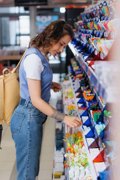 Side view of woman in jeans trying new ball pen in stationery store - foto de stock