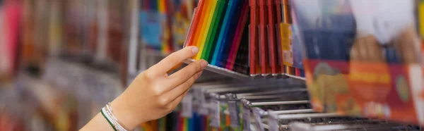 Partial view of woman in beaded bracelets holding set of multicolored felt pens in blurred shop, banner - foto de stock