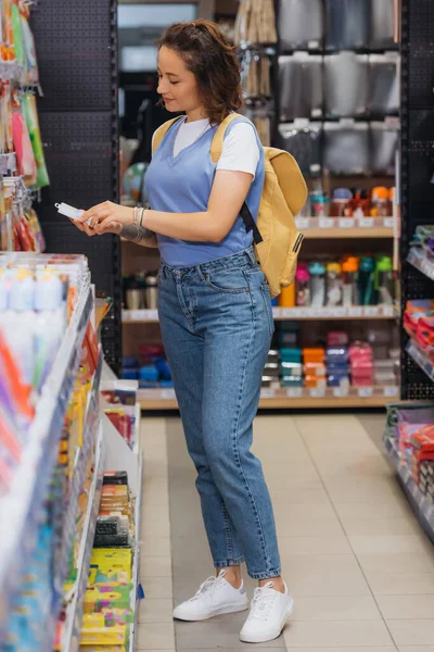 Full length of woman in jeans choosing new stationery in store — Photo de stock