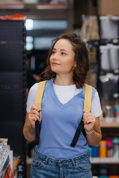 Young brunette woman with backpack smiling in stationery store - foto de stock
