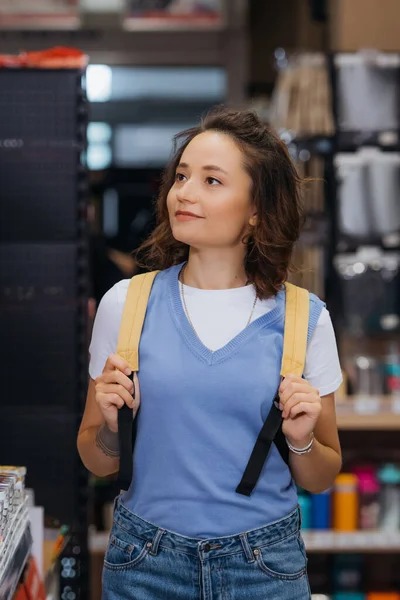 Young brunette woman with backpack smiling in stationery store — Stockfoto