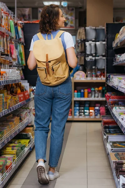 Back view of student with backpack walking along racks in stationery store — Stock Photo