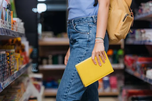 Ausgeschnittene Ansicht eines Studenten in Jeans und Perlenarmbändern, der ein neues Werbebuch im Laden hält — Stockfoto