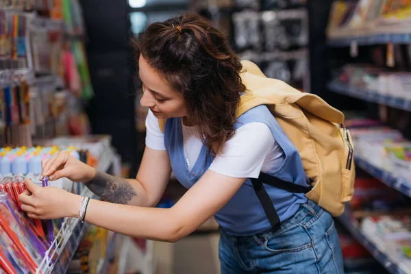 Junge Studentin mit Rucksack wählt Filzstifte im Schreibwarengeschäft — Stockfoto