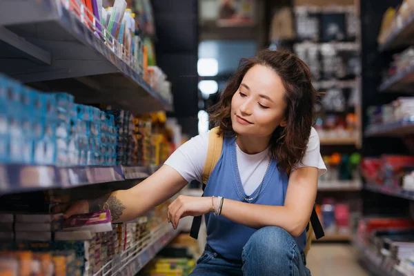 Tätowierte Studentin wählt Zettel auf Regal im Schreibwarengeschäft — Stockfoto