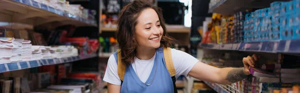 Junge Frau lächelt in der Nähe von Regalen mit Textbüchern und Zetteln, Banner — Stockfoto